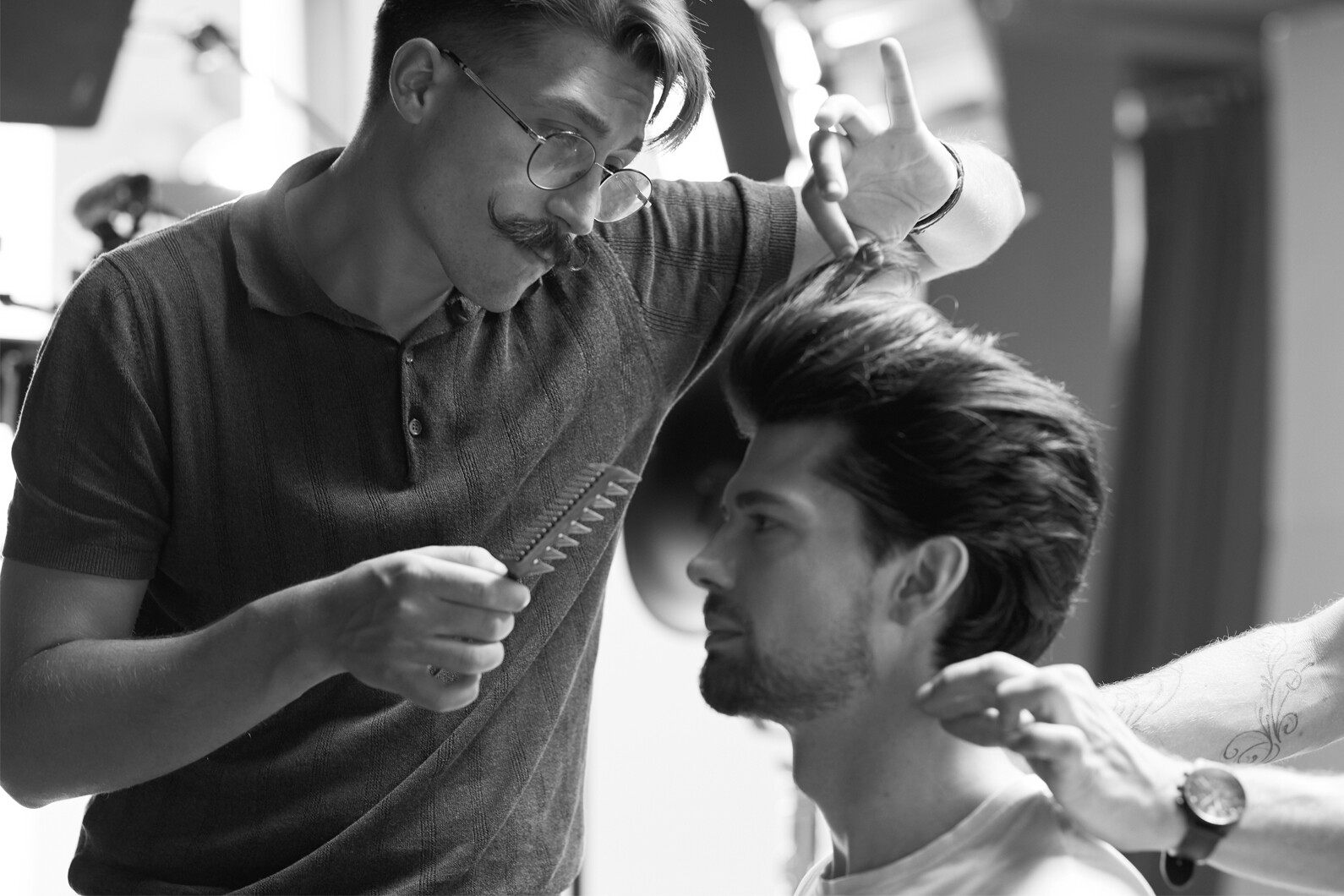 ein Friseur hält einen Kamm in der rechten Hand und zupft mit der linken Hand eine Haarsträhne bei einem Mann zurecht